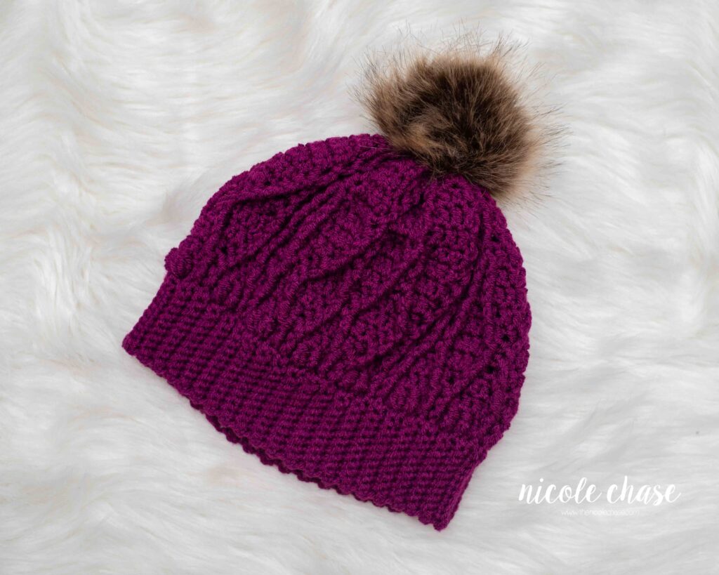 magenta colored crochet cable beanie with a brown faux fur pom
